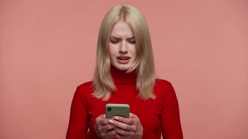Woman Reading Upsetting Message on Smartphone on Pink