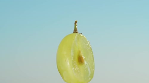 Half of a green grape with a stone, rotates against a blue sky background, close-up