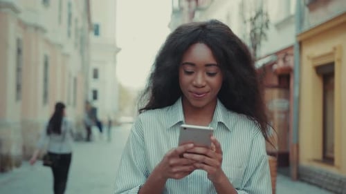 Cheerful Young Woman Walks in the City Uses Her Smarpthone for Online Messaging Sending Sms Being
