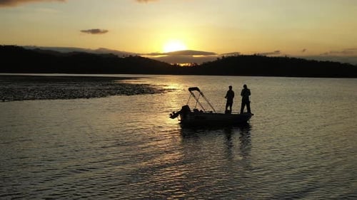 4K Aerial Drone Flyover With Silhouette Of Men Fishing And Casting Off Boat On A Lake At Sunset