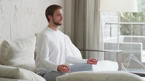 Mindfulness and Calm Mood Young Man Sits on a Sofa in the Living Room and Meditates a Calm Mood