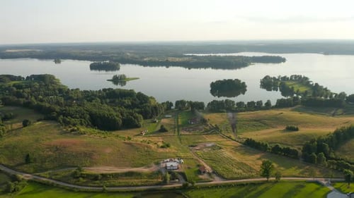 Drone flying by the countryside lake with green nature surrounding.