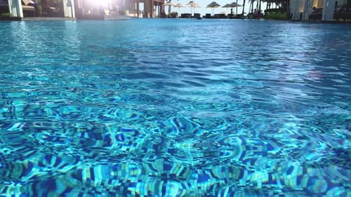 Cool refreshing water in a swimming pool with silhouette of people and shade umbrellas in the backgr