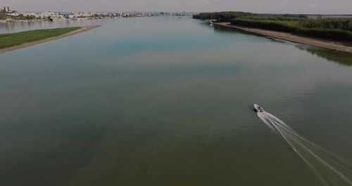 Revealing drone shot lone person sails a small inflatable boat along a big calm river. City skyline