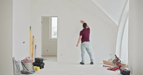 Man Sands Wall in Brightly Lit Room