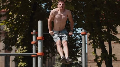 Muscular Man Doing Pull-Ups and Dips in Park