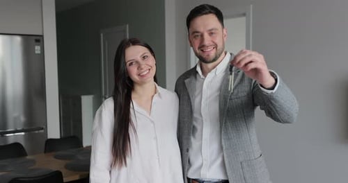 Happy Married Couple Owners of a New Apartment Show the Key Looking at Camera Wife and Husband Hug