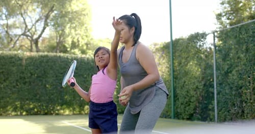 Teaching tennis, woman instructing girl holding racket on court outdoors