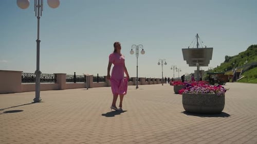 Elegant Female in Pink Attire Explores Seaside Promenade Under Sunny Sky Graceful Woman Dressed in