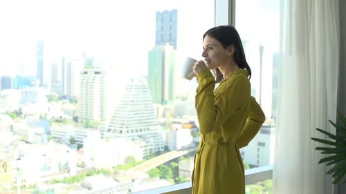 Young Woman Admire View From Window and Drinking Coffee 30s