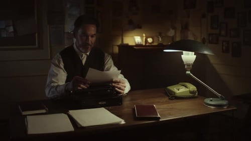 Man Typing at Vintage Typewriter Under Lamp Light