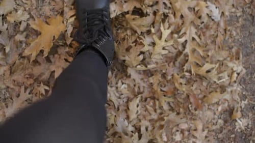 Woman's boots walking through dead, dried, autumn leaves - straight down first person view