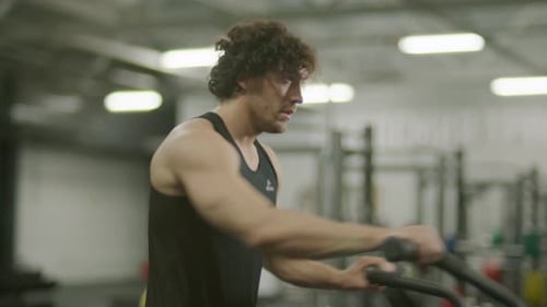 Strong Man Exercising on Air Bike during Fitness Session at Gym