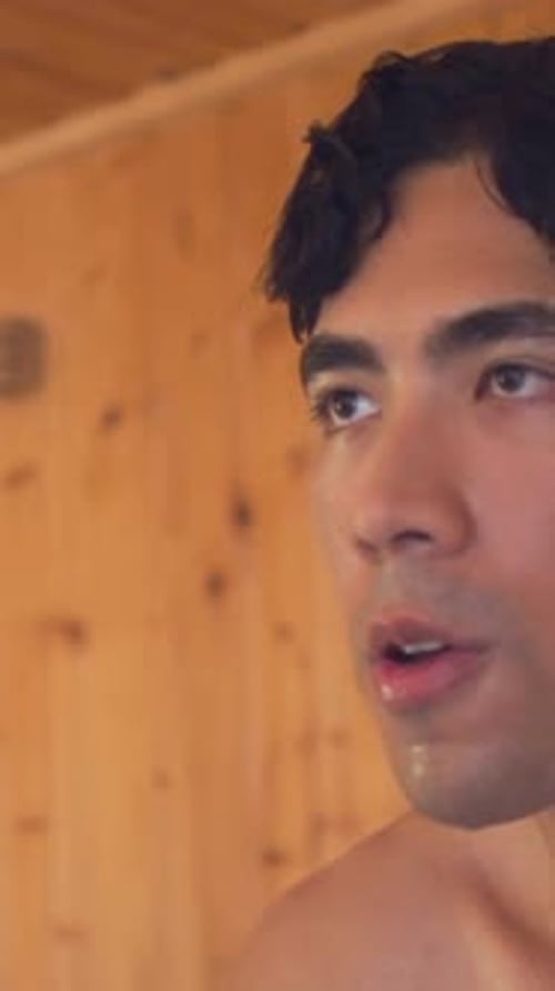 Vertical video: Heat causing shirtless man breathing in cabin, glancing up right, moist skin, vent