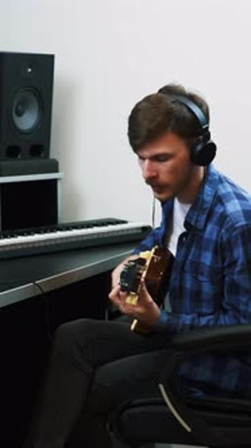 Man in headphones playing on guitar and recording song at studio. Vertical video