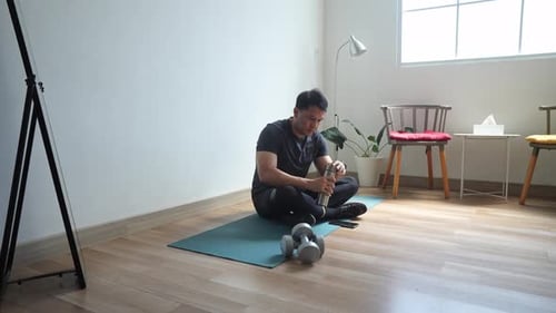 Man Drinking Water and Looking at Phone After Workout