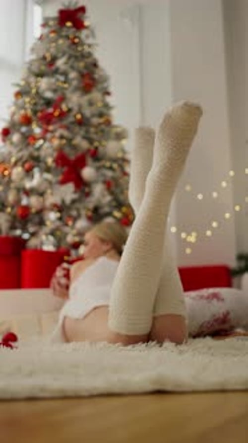 Woman Lying by Christmas Tree in Cozy Socks