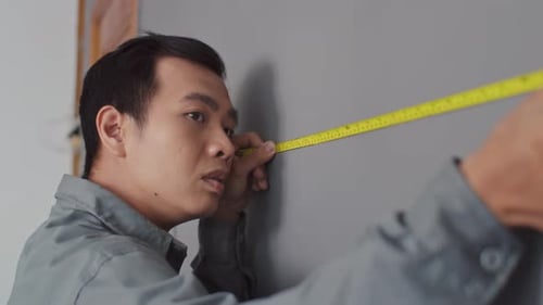 Builder Measuring Wall with Tape Measure