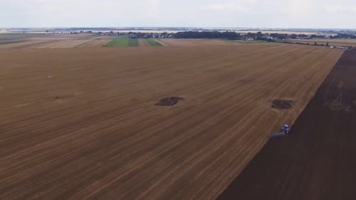 Blue Modern Plowing Tractor Working In The Field. Aerial Dolly-Out Shot.