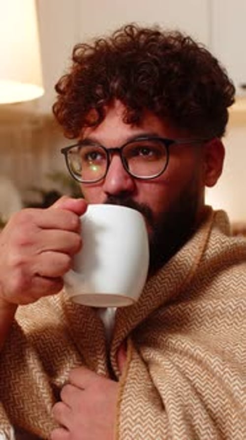 Man with Blanket Drinks from Mug at Home