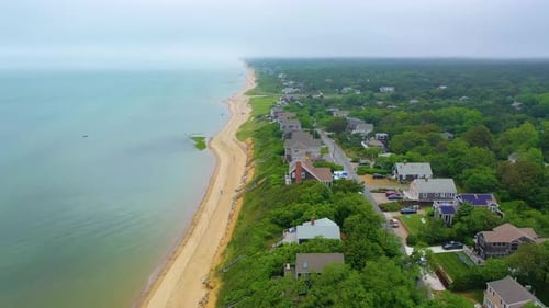 Cape Cod beach houses along shoreline at high tide with drifting boat and stormy skies above