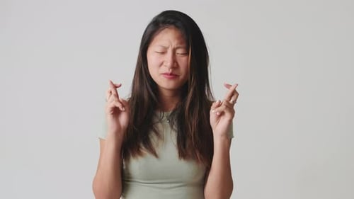 Young woman fingers crossing and wishing best isolated over white background in studio