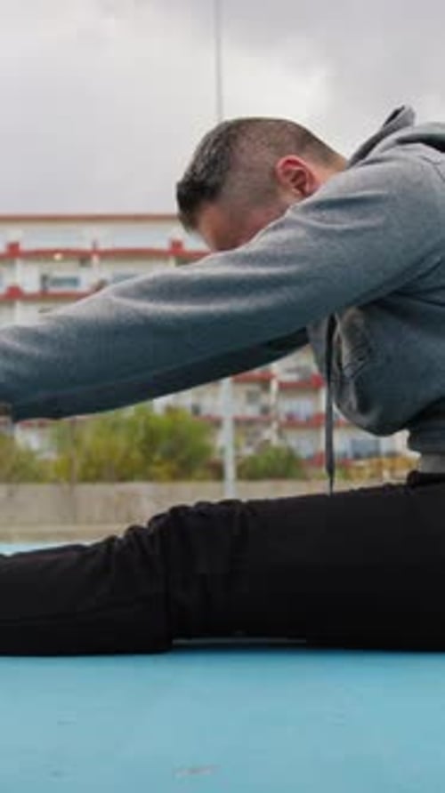 Sporty Athlete Man Does Stretching While Sitting In Sports Field