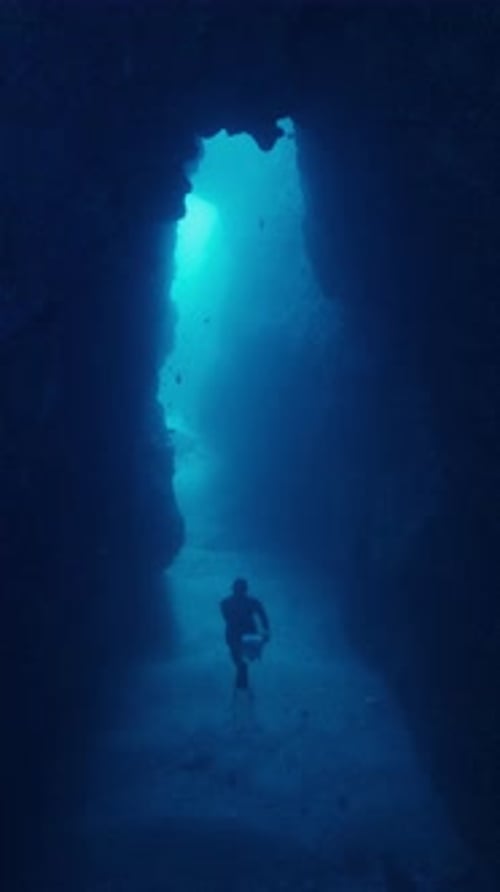 Apnéiste professionnel explorant une grotte sous-marine sombre avec une entrée lumineuse