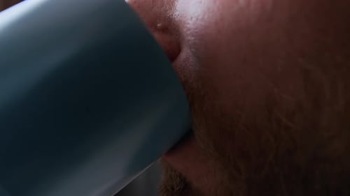 Man with red beard drinking from a blue cup