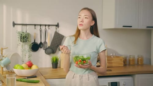 Portrait of young Caucasian girl eating green salad in kitchen at home.