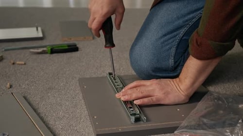 Des mains masculines fixent la glissière au panneau du tiroir à l'aide d'un tournevis pendant l'assemblage