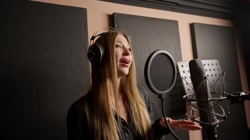 girl singer singing in a recording studio with headphones in front of microphone to create a song