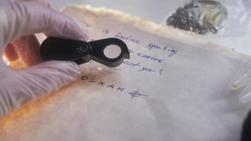 Die Hand eines forensischen Detektivs, der eine Lupe hält, untersucht einen handgeschriebenen Brief aus dem Tierkreis
