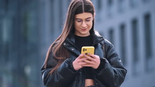 Young woman is outdoors near building is holding smartphone