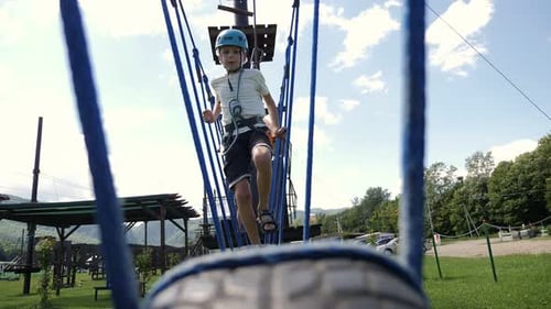 A Little Boy in a Hard Hat Passes Obstacles on a Cable Car in an Adventure Park