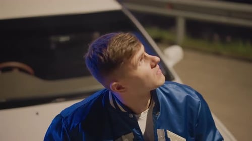 Man leaning against car looks up at night