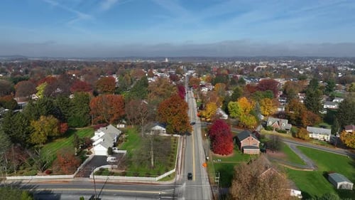Small town in USA residential district. Descending aerial of car driving on road. Autumn fall foliag