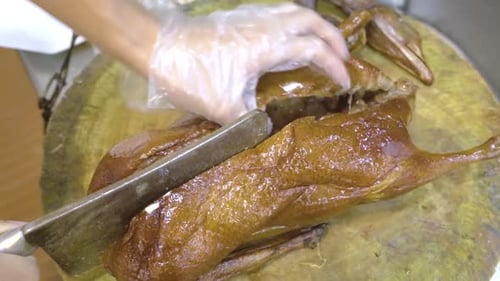 Man Cutting A Roasted Goose Into Half With A Butcher's Knife In Guangzhou, China - close up