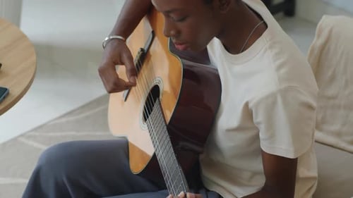 Young Adult Plays Guitar Indoors During the Day