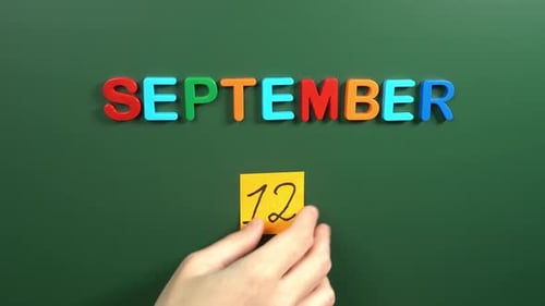 Hand sticking a sticker 12 September calendar day on school board. 12 date of September. Twelfth