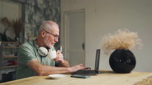 Senior Man Working on Laptop at Wooden Table