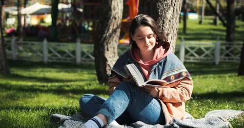 Portrait of Cheerful Young Woman Reading Book in the Park Reading Outside in Spring Sunlight Girl