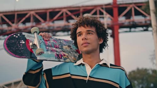 Relaxed Skater Walking Embankment Portrait. Young Man Holding Longboard on Shoulders Closeup