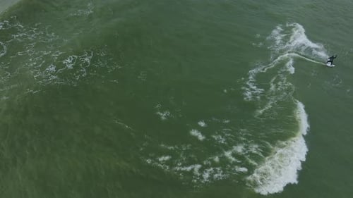 Establishing aerial birdseye view of a man engaged in kitesurfing, overcast winter day, high waves,