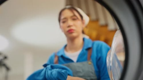 Front view of Asian housekeeper or housemaid put cloth into washing machine during home service