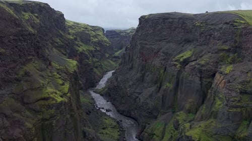 Cinematic drone flight through a jagged mossy canyon with a winding river below.