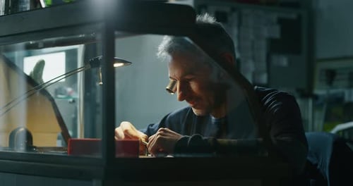 Man Repairing Electronics Device at Workbench Under Lamp