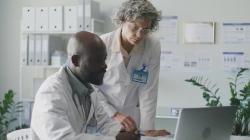 Two Doctors Discussing Treatment Plan on Laptop Screen in Medical Office