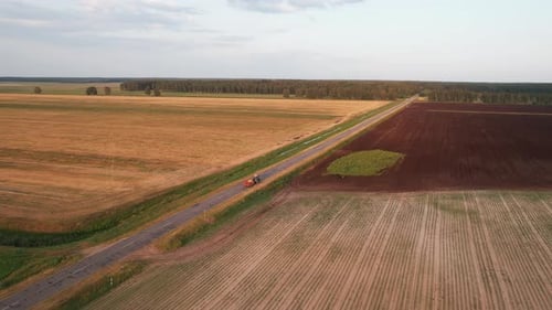 Aerial View of Plowed Land and Fields with Cereals and a Tractor with a Hindcarriage on an Asphalt