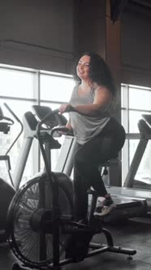 Joyeuse femme de grande taille faisant du vélo à air dans une salle de sport lumineuse